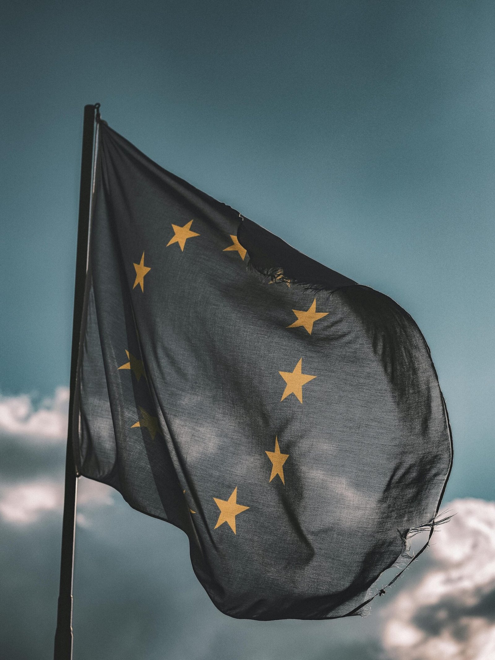 img-03-free-img European Union flag gently waving on a flagpole against a cloudy sky, symbolizing unity and patriotism.